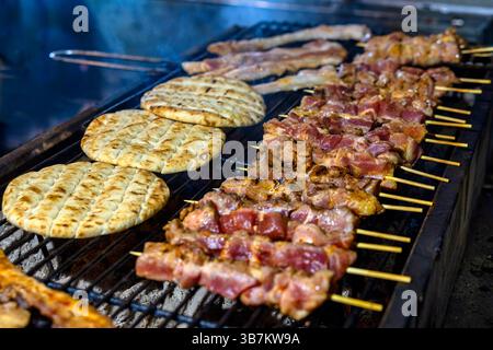 Gegrillte Fleischspieße, die über heißen Kohlen sickern, neben warmem, geröstetem Pita-Brot – ein unwiderstehlicher Geschmack mediterraner Street Food Stockfoto