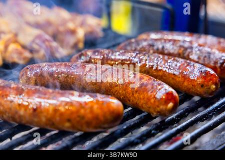 Saftige Würstchen, die auf dem Grill brüsten, mit goldener, knuspriger Haut und rauchigen Aromen, die die Luft füllen – perfekt für jeden Happen. Stockfoto