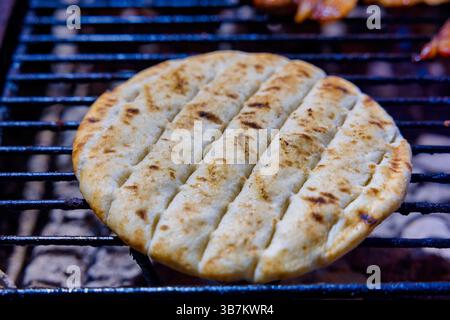 Ein Stück Fladenbrot wird gegrillt, das knackige Grillspuren aufweist. Die goldbraune Oberfläche hebt die Textur hervor und fängt einen köstlichen Kochmoment ein Stockfoto