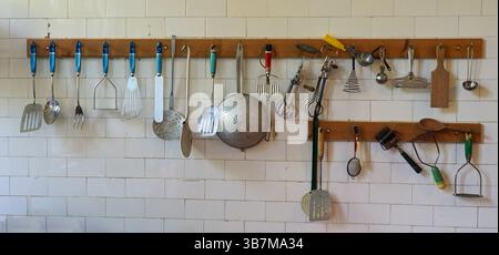 Alte Kochutensilien hängen an der gefliesten Küchenwand. Stockfoto
