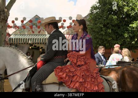 Andalusisches Paar zu Pferd auf der Feria de Sevilla 2025, gekleidet in eleganter traditioneller Kleidung mit Flamenco-Rüschen und klassischem spanischem Stil. Stockfoto