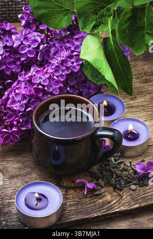 Duftender Frühlingsblumentee auf dem Hintergrund brennender Kerzen und Fliederstrauß Stockfoto
