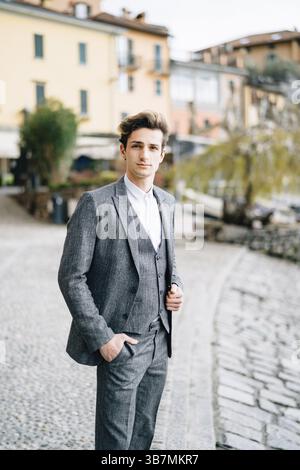 Der Bräutigam steht auf dem Kopfsteinpflaster der Straße in Varenna vor dem Hintergrund alter Villen. Comer See. Stockfoto