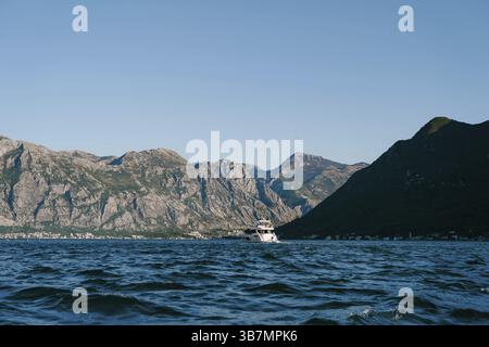 Das Boot schwimmt auf dem blauen Meer vor der Kulisse einer hohen Bergkette. Stockfoto
