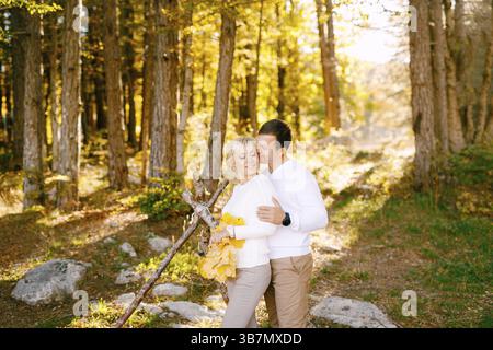 Der Mann küsst und umarmt die lächelnde Frau an den Schultern. Die Frau hat gelbe Blätter in den Händen. Weitwinkel. Stockfoto