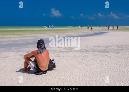 Holbox, Mexiko – 10. Februar 2025: Ein sonnenverbrannter Mann macht eine Pause auf der unberührten Sandbank in der Nähe von Punta Mosquito, umgeben von der türkisfarbenen Karibik Stockfoto