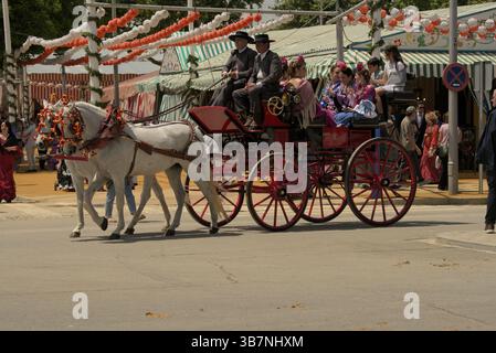 Dekorierte Pferdekutsche mit Flamenco-gekleideten Passagieren während La Feria de Sevilla 2025 in Andalusien. Feria de Sevilla, Spanien Stockfoto