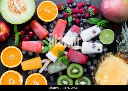 Auf einem Bett aus frischen Früchten, darunter Kiwi, Melonen und Zitrusfrüchten, steht eine bunte Auswahl an Eiscremepieps mit Beerengeschmack. Stockfoto