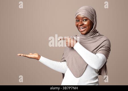 Aktivieren Sie Diese Option. Aufgeregt Schwarze Frau In Hijab Zeigt Auf Ihre Leere Handfläche Stockfoto
