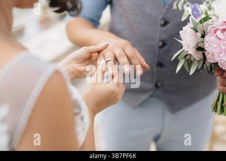 Die Braut legt den Ring während der Hochzeitszeremonie auf den Finger des Bräutigams. Stockfoto