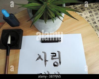 Nahaufnahme der noch feuchten koreanischen Kalligraphie mit einem traditionellen Pinsel auf weißem Papier, der Hangul-Zeichen zeigt Stockfoto