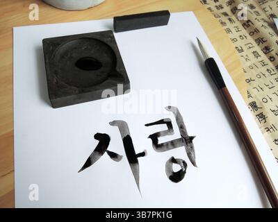 Nahaufnahme der noch feuchten koreanischen Kalligraphie mit einem traditionellen Pinsel auf weißem Papier, der Hangul-Zeichen zeigt Stockfoto