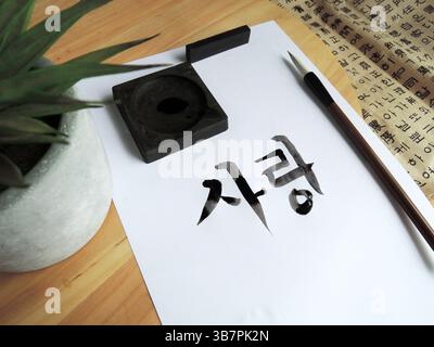 Nahaufnahme der noch feuchten koreanischen Kalligraphie mit einem traditionellen Pinsel auf weißem Papier, der Hangul-Zeichen zeigt Stockfoto