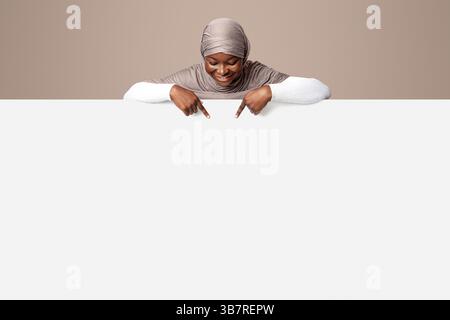 Aktivieren Sie Diese Option. Afrikanische muslimische Dame in Hijab zeigt auf weiße Werbetafel Stockfoto