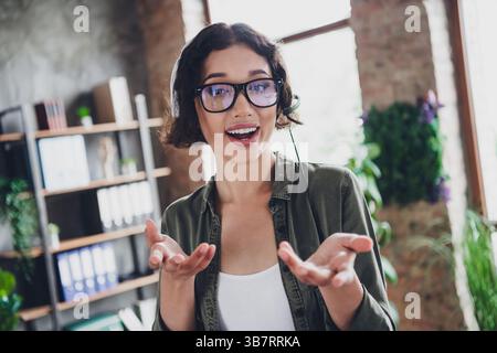 Junge Frau im legeren Outfit, die ein Headset trägt, in einem modernen Büro arbeitet, lächelt und sich in der Kommunikation engagiert Stockfoto