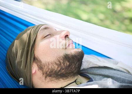 Porträt eines jungen Mannes, der friedlich in einer Hängematte schläft, draußen an einem sonnigen Tag. Sein Ausdruck vermittelt Ruhe und Wohlbefinden. Stockfoto