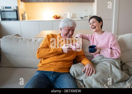 Glückliche lachende Ehemann- und Ehefrau-Paare, die gemeinsam auf einer gemütlichen Couch im Wohnzimmer Tee genießen Stockfoto