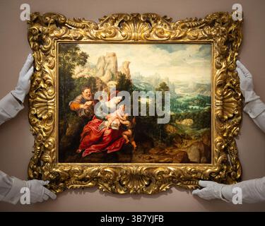 28. Juni 2024, London, England, Vereinigtes Königreich: Die Mitarbeiter von Sotheby's halten „die Heilige Familie mit dem Säugling Johannes dem Täufer in einer ausgedehnten Landschaft mit Reisenden“ von Herri Met de Bles und Sir Peter Paul Rubens, geschätzt auf 600.000 bis 800.000 GBP, während des Fotorufs für Sothebyâ Old Masters Sale in London. (Foto: © Thomas Krych/ZUMA Press Wire) Stockfoto
