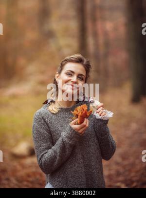 Attraktive Frau mit geflochtenen Zöpfen hält im Herbstwald gefallene Blätter in den Händen. Herbstkunstporträt Stockfoto