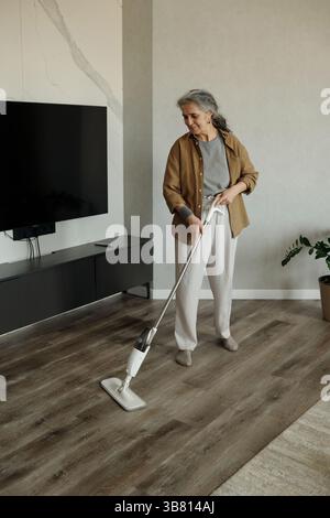 Ältere Frau, die im Wohnzimmer Steam Mopp auf Hartholzboden benutzt Stockfoto