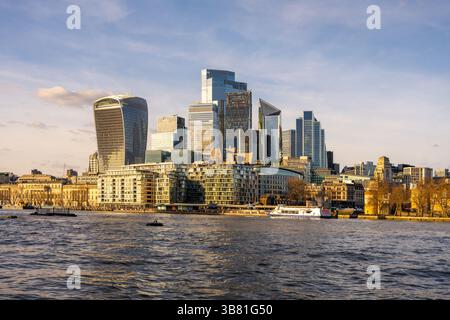 Die Skyline von London verfügt über moderne Wolkenkratzer, die den warmen Glanz des Sonnenuntergangs reflektieren. Die Themse fließt friedlich, eingerahmt von eleganter Architektur und Gebäuden am Fluss. Stockfoto