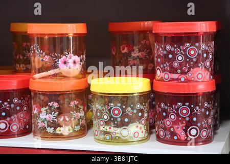 Eine Nahaufnahme auf Augenhöhe zeigt eine Reihe von farbenfrohen Plastikgläsern mit Deckel, die mit Blumen- und Kreismustern versehen sind und ordentlich auf einer weißen Oberfläche angeordnet sind Stockfoto