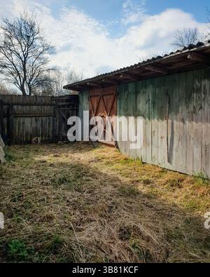 Leerer Hof mit Heu bedeckt, alte Holzscheune. Sonniges Wetter und Himmel mit wenigen Wolken. Stockfoto