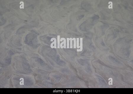 Die Vollformataufnahme zeigt strukturierten, welligen Sand an einem grauen Strand und kreiert faszinierende wellenartige Muster und ein abstraktes Meeresgefühl mit dezentem Li Stockfoto