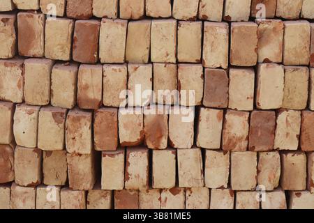 Das Bild zeigt eine Nahaufnahme von gestapelten Ziegeln in horizontalen Reihen, wodurch ein texturierter Hintergrund entsteht. Die Baumaterialien aus rotem Ton sind ordentlich arr Stockfoto