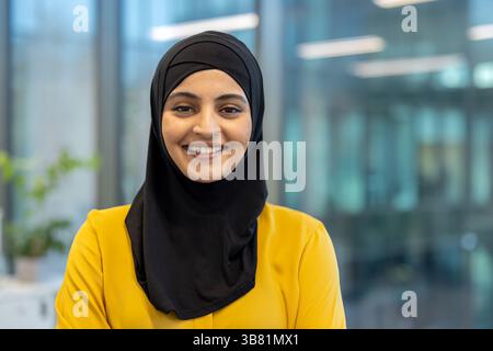 Eine lächelnde, schöne Frau mit schwarzem Hijab und gelber Bluse blickt direkt in die Kamera. Stockfoto