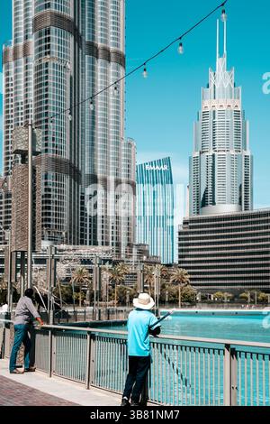 Dubai, VAE - 30. April 2026: Asiatischer Migrant Worker auf den Straßen von Dubai. Hochwertiges fotooffenes Bild eines asiatischen Arbeitsmigranten, der auf einer Straße in Dubai, Vereinigte Arabische Emirate, spaziert. In Arbeitskleidung unter der intensiven Sonne des Nahen Ostens verkleidet, repräsentiert der Mann die hart arbeitenden Einwanderer, die die rasante Stadtentwicklung der Stadt unterstützen. Das Foto zeigt Themen wie Globalisierung, Arbeitsmigration und Alltag in einer modernen Metropole. Stockfoto