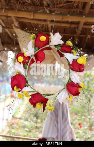 Aus nächster Nähe zeigt ein kreisförmiger Kranz die Schönheit von Rosen, Chrysanthemen und weißen Blumen, die auf einem zarten Rahmen angeordnet sind; erinnert an natürliche Eleganz und Stockfoto