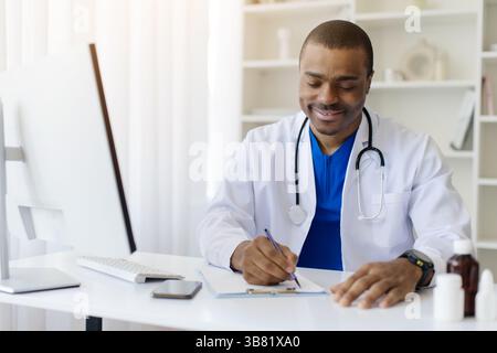 Afroamerikaner Arzt schreibt auf Klemmbrett, während er am Schreibtisch im Büro sitzt Stockfoto