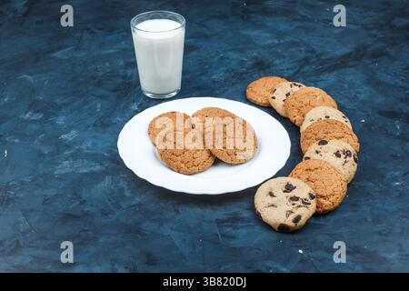 Erdnussbutter-Kekse in weißer Platte mit Milch, verschiedene Arten von Keksen auf dunkelblauem Hintergrund. Horizontal Stockfoto