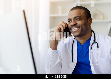 Afroamerikaner Arzt lächelt, während er am Arbeitsplatz am Handy spricht Stockfoto