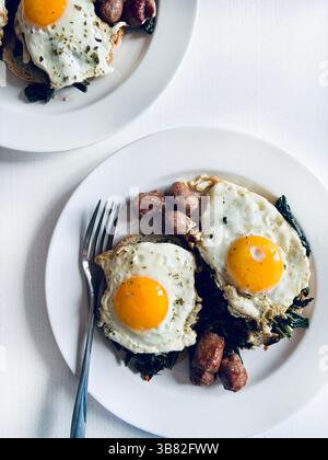 Zwei Spiegeleier mit Wurst und gekochtem Gemüse auf einem weißen Teller auf einem weißen Tisch. Direkt darüber. Stockfoto