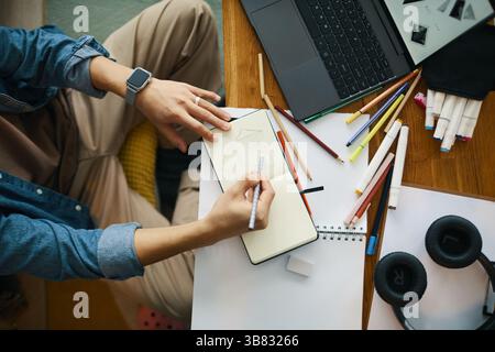 Mann arbeitet mit detaillierter Präzision an architektonischen Skizzen mit verschiedenen Zeichenwerkzeugen und einem Laptop auf dem Schreibtisch, wobei er sich auf die Desi konzentriert Stockfoto