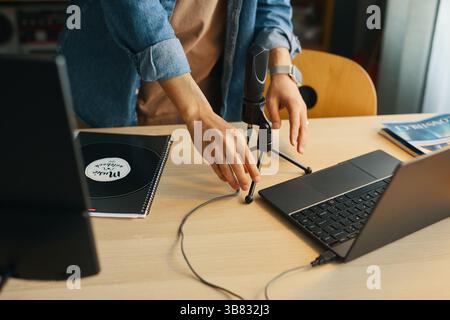 Nahaufnahme von männlichen Händen, die das Mikrofon auf dem Schreibtisch einstellen, während Sie Laptop und Notebook verwenden. Bericht auf dem Schreibtisch, Person, die an einer aktiven Arbeitssitzung beteiligt ist Stockfoto