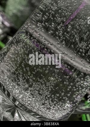 Nahaufnahme eines mit kohlensäurehaltigem Wasser gefüllten Klarglases, das eine detaillierte Ansicht von sprudelnden Blasen zeigt, die durch die Flüssigkeit steigen. Stockfoto