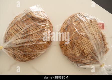 Zwei Brotlaibe, die ordentlich in eine durchsichtige Kunststoffverpackung gewickelt sind, stehen nebeneinander auf einer sauberen, hellen Oberfläche. Sichtbare Textur und gleichmäßige Struktur Stockfoto