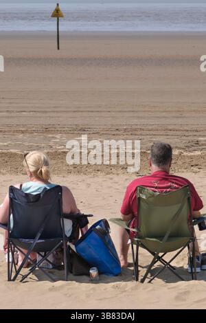 Zwei Personen saßen auf der Promenade von weston-super-nare und genossen die Strandliegen am Meer; Klappstühle; Stockfoto