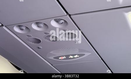 Overhead aircraft control panel showing circular vents and illuminated seatbelt and no smoking signs. Stockfoto