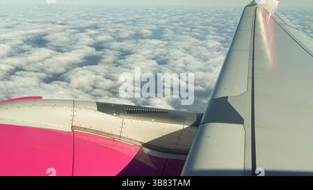 Luftaufnahme vom Flugzeugflügel über eine wunderschöne Wolkenlandschaft am sonnigen Tag mit leuchtendem rosa und grauen Flugzeugflügel mit glatten Wolken. Stockfoto
