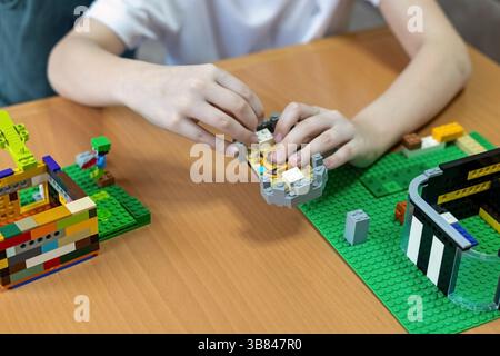 Kind baut kreative Backsteinstrukturen auf dem Tisch. Nahaufnahme eines Kindes Hände, die bunte Plastikziegel auf einem Holztisch zusammensetzen und dabei mitmachen Stockfoto