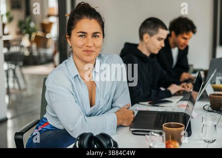 Porträt einer lächelnden jungen Geschäftsfrau, die im Büro am Tisch sitzt Stockfoto
