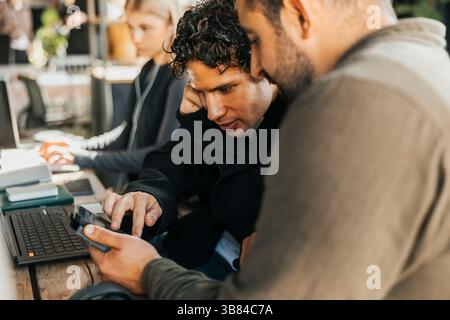 Männliche Software-Ingenieure verwenden Smartphones, während sie Strategien im Technikbüro diskutieren Stockfoto