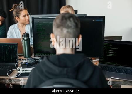Rückansicht eines nicht binären Softwareentwicklers, der Computer zur Programmierung verwendet, während er HTML-Analysen im TECH-Hub analysiert Stockfoto
