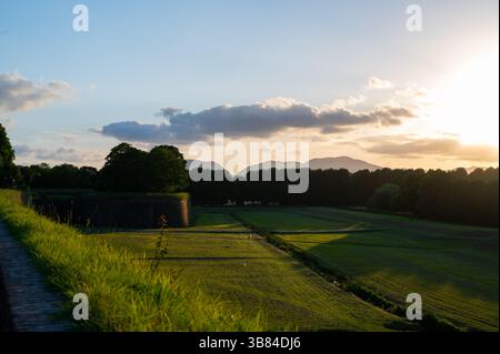 Sonnenuntergang über der Stadt Lucca, Toskana, von den historischen Mauern aus gesehen. Die Sonne untergeht hinter den toskanischen Hügeln und wirft ein goldenes Leuchten über Dächer und Stockfoto