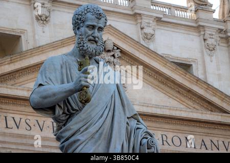 Die monumentale Statue des Heiligen Peter auf dem Petersplatz im Vatikan. Im Hintergrund die Fassade des Petersdoms. Halblange Länge Stockfoto