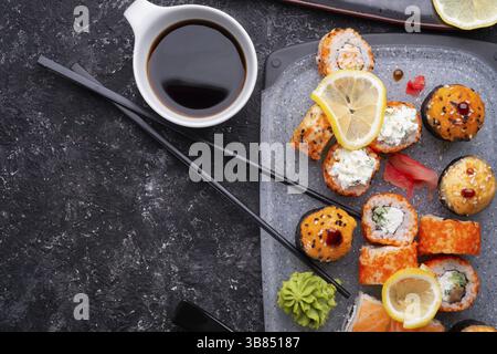 Sushi-Brötchen auf grauem Tablett am schwarzen Tisch. Flache Lagen Stockfoto